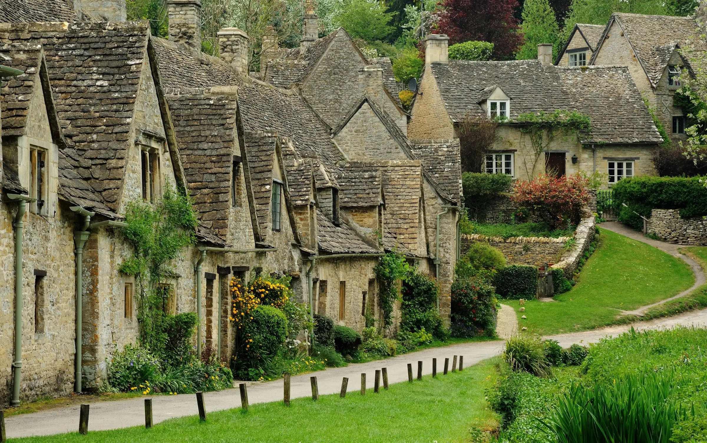 Arlington Row in Bibury: a terrace of honey-coloured Cotswold stone cottages with steep stone-tiled roofs above a green bank