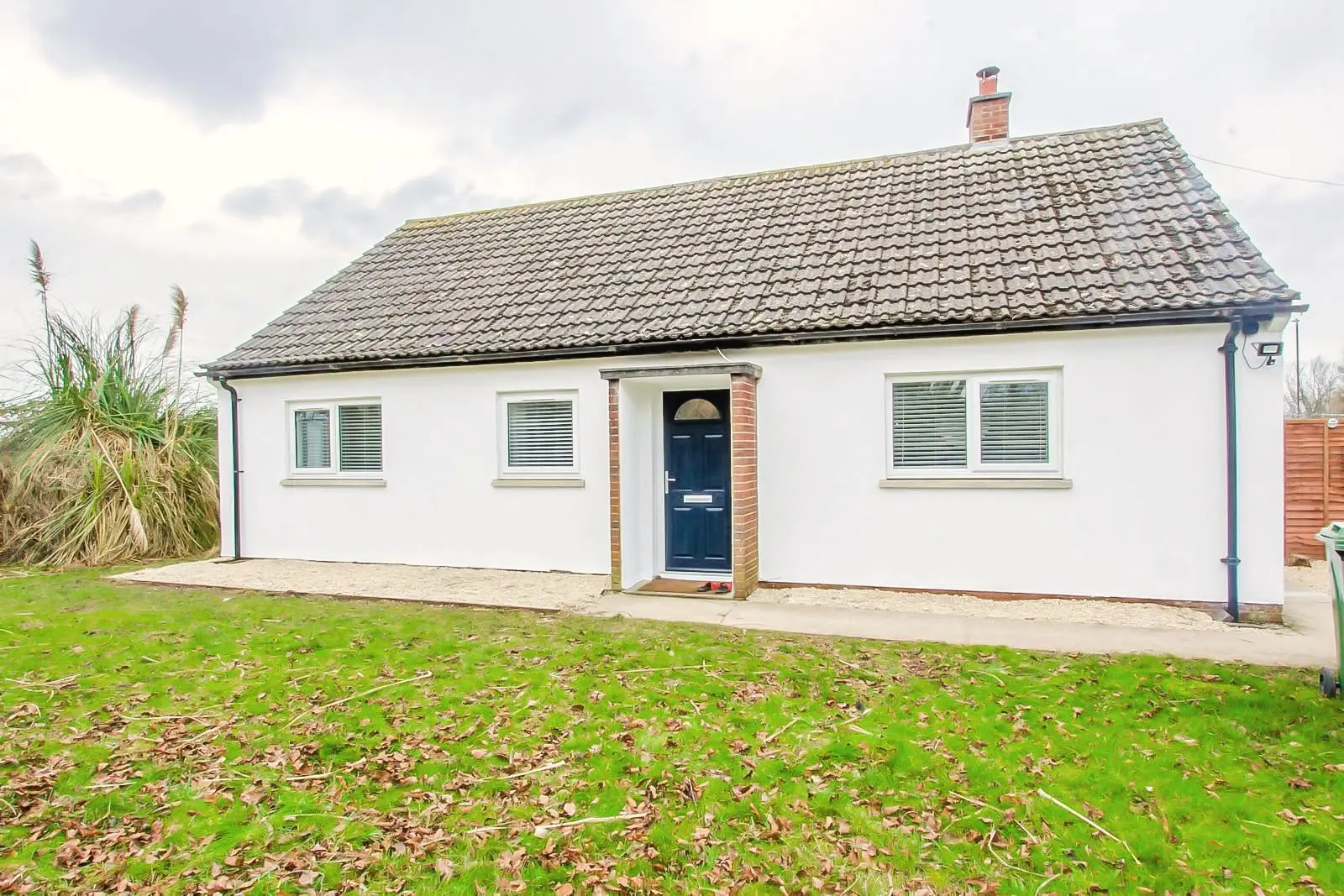 A white three-bedroom bungalow with a navy front door and a lawn in front