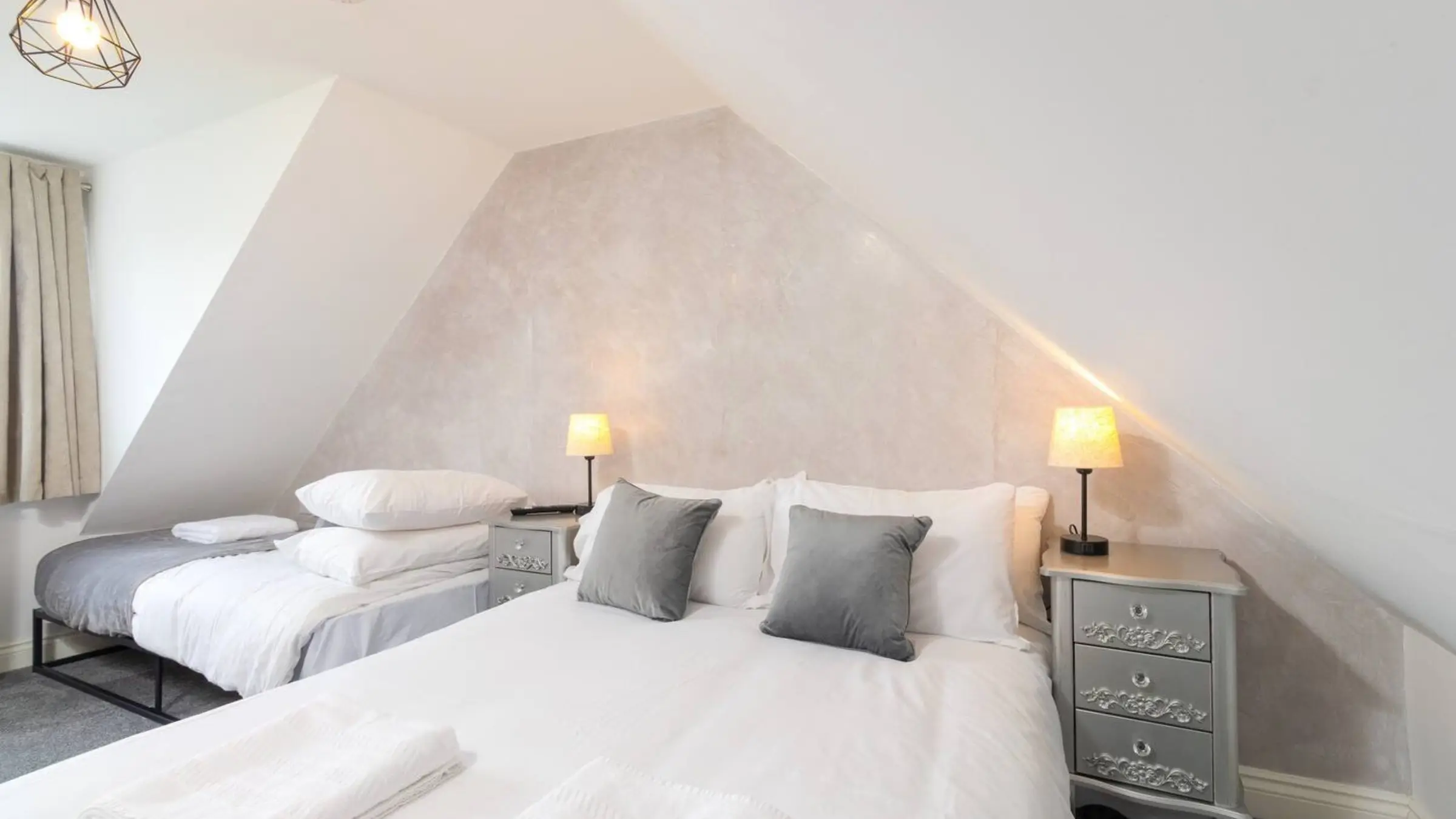 A bedroom made up for two guests on a work stay: a double bed and a single, fresh towels and bedside lamps under a sloping ceiling
