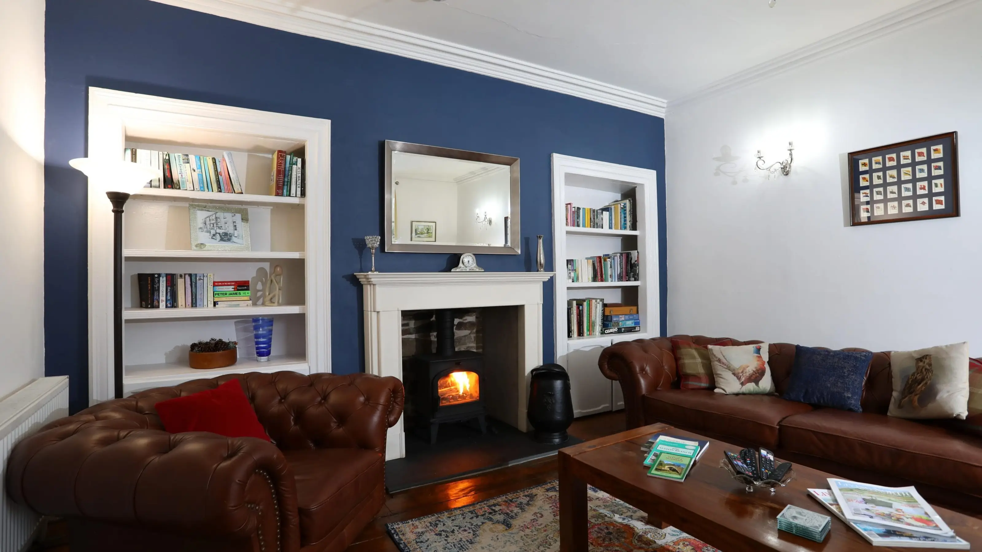 A guest-ready holiday-let lounge with a lit wood burner, leather sofas and bookshelves