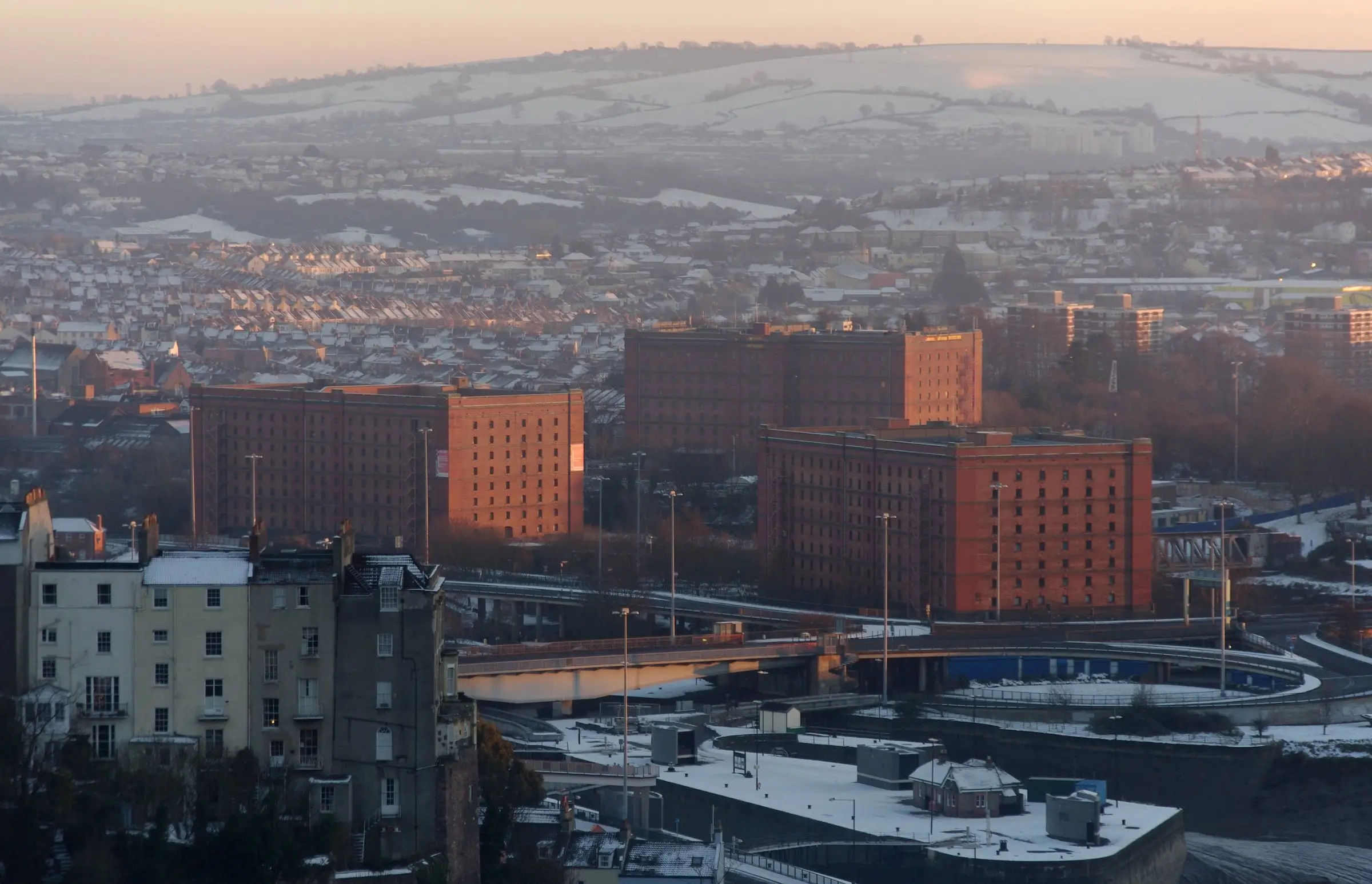 Bristol at a frosty winter dawn, the red-brick bonded warehouses and rows of terraces lit pink below snow-covered hills