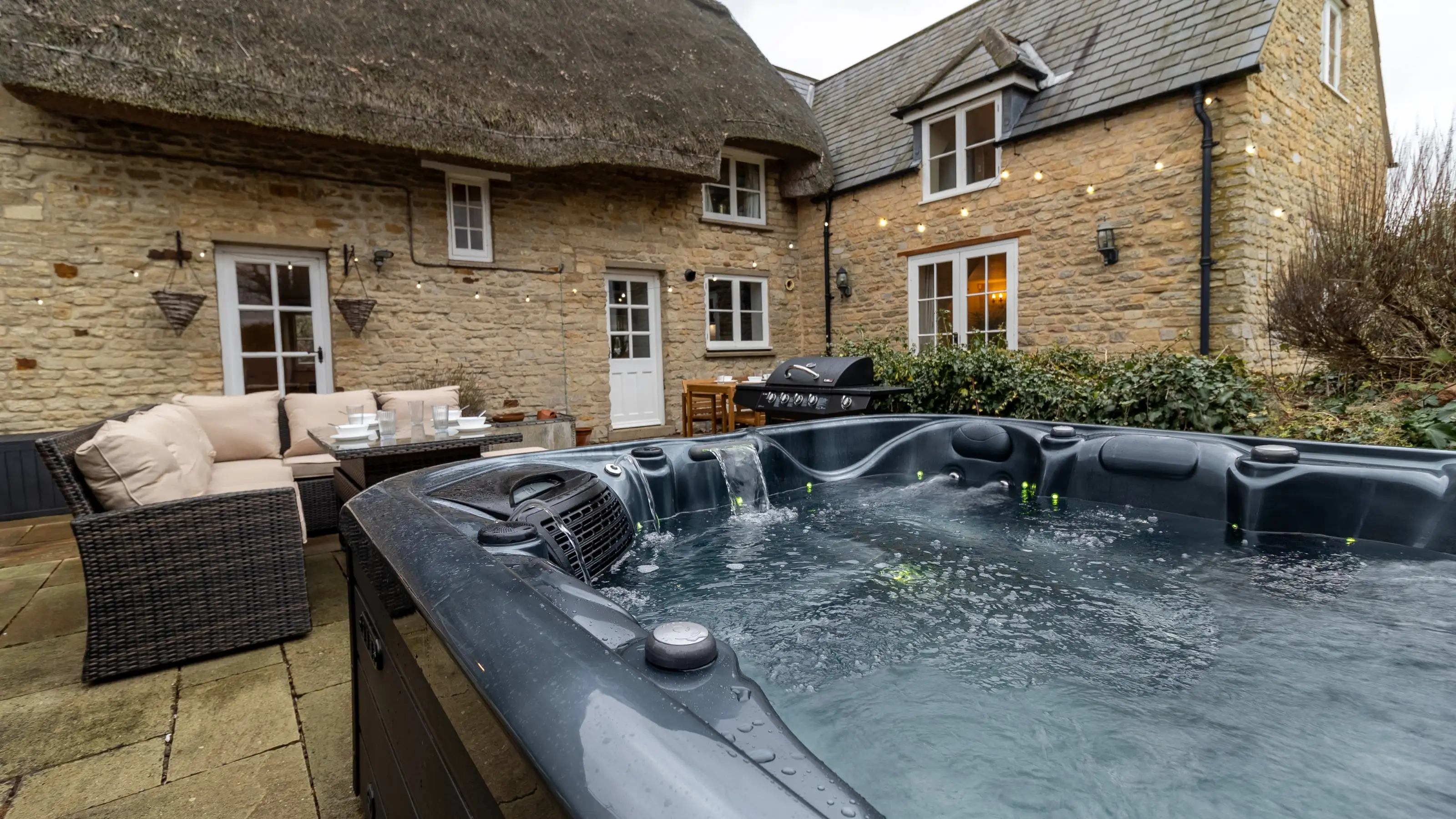Thatched stone holiday cottage with a hot tub, festoon lights and outdoor seating, the kind of stay guests book again and again