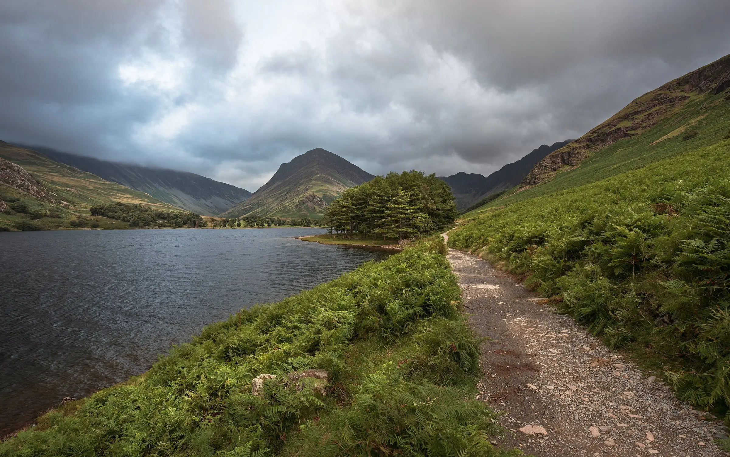A lakeside path through bracken under a grey autumn sky, fells rising behind the water