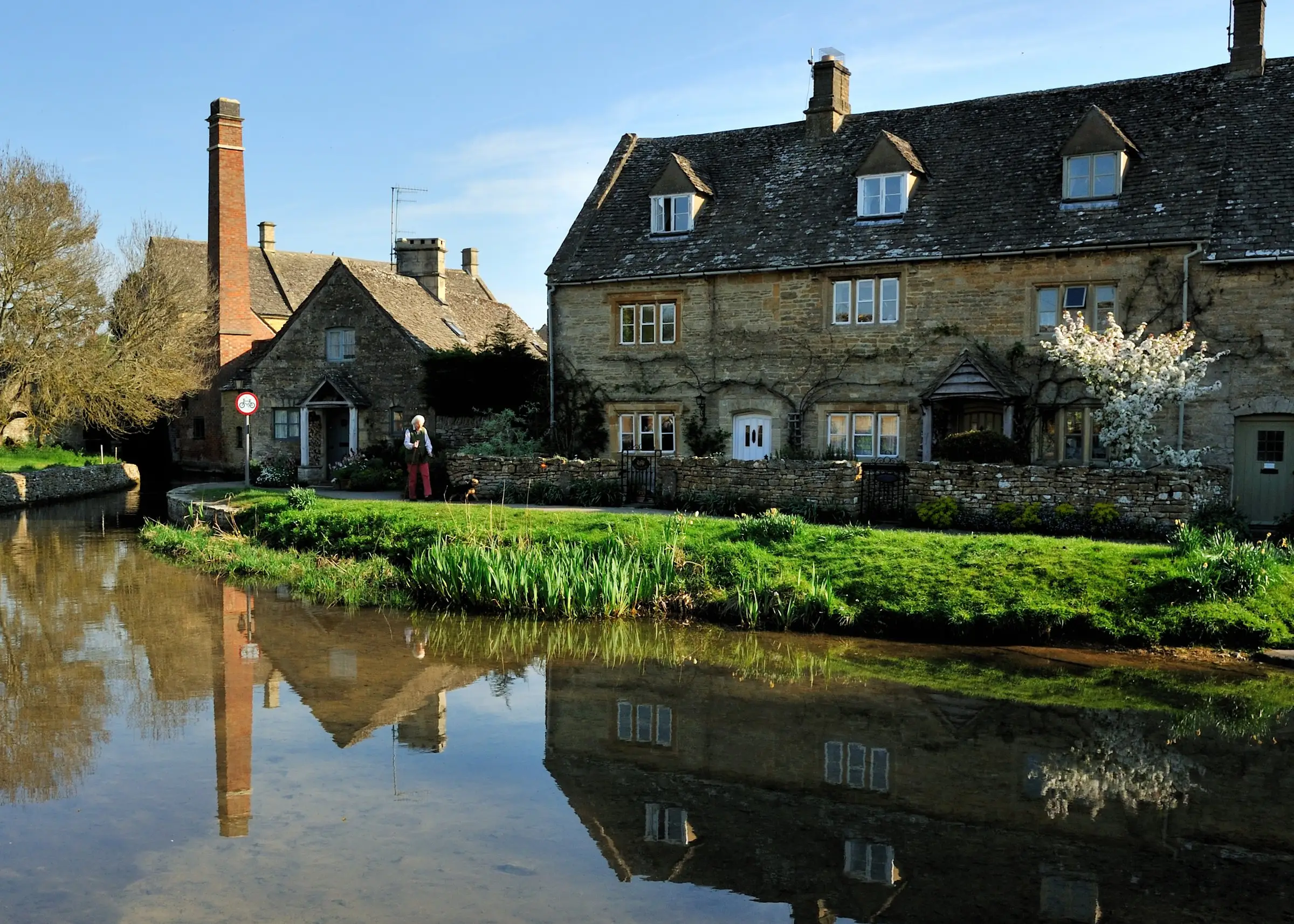 Stone cottages in Lower Slaughter in low evening light, reflected in the still water of the River Eye