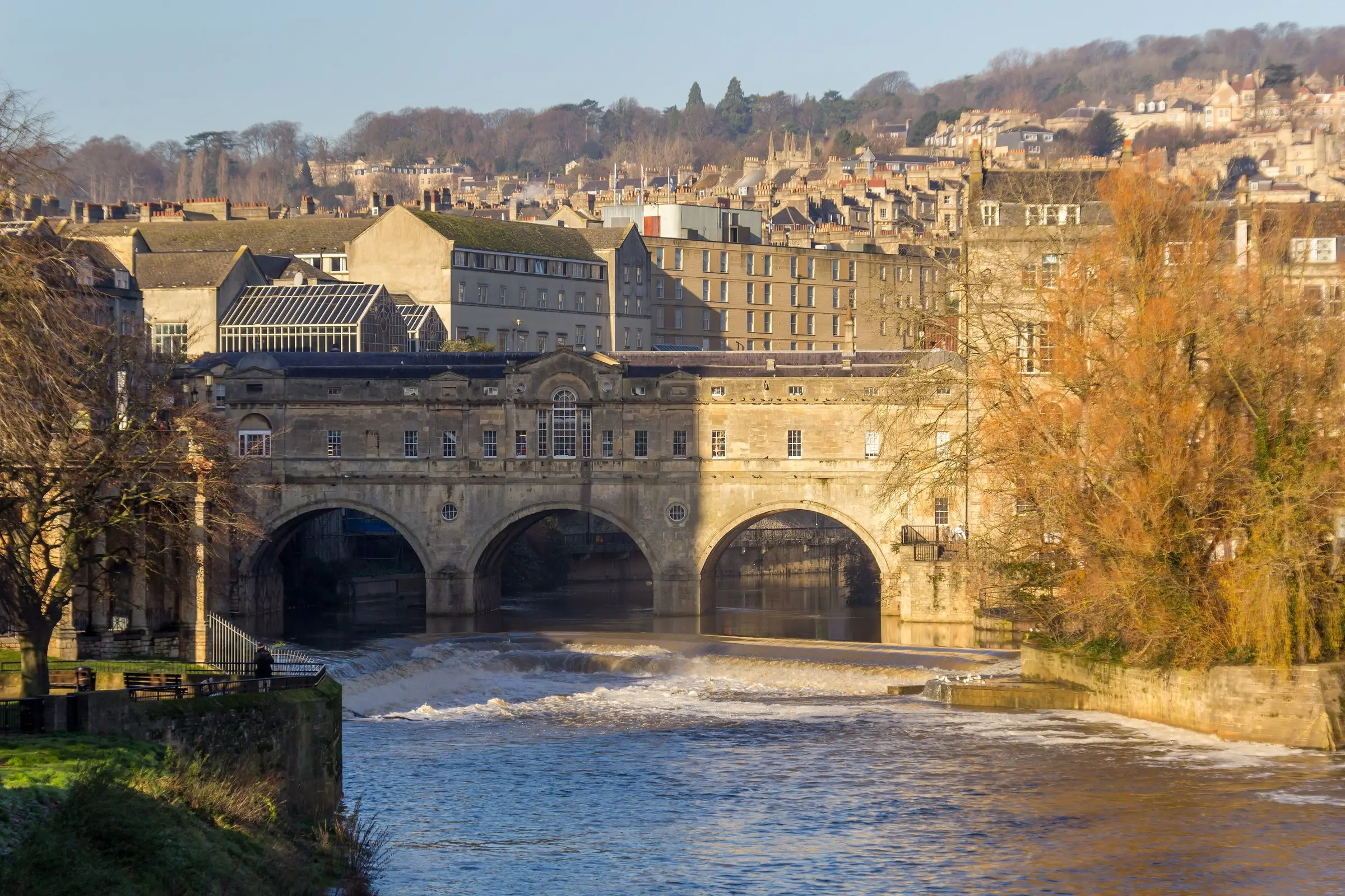 Pulteney Bridge and the weir on the River Avon in Bath, autumn trees along the bank