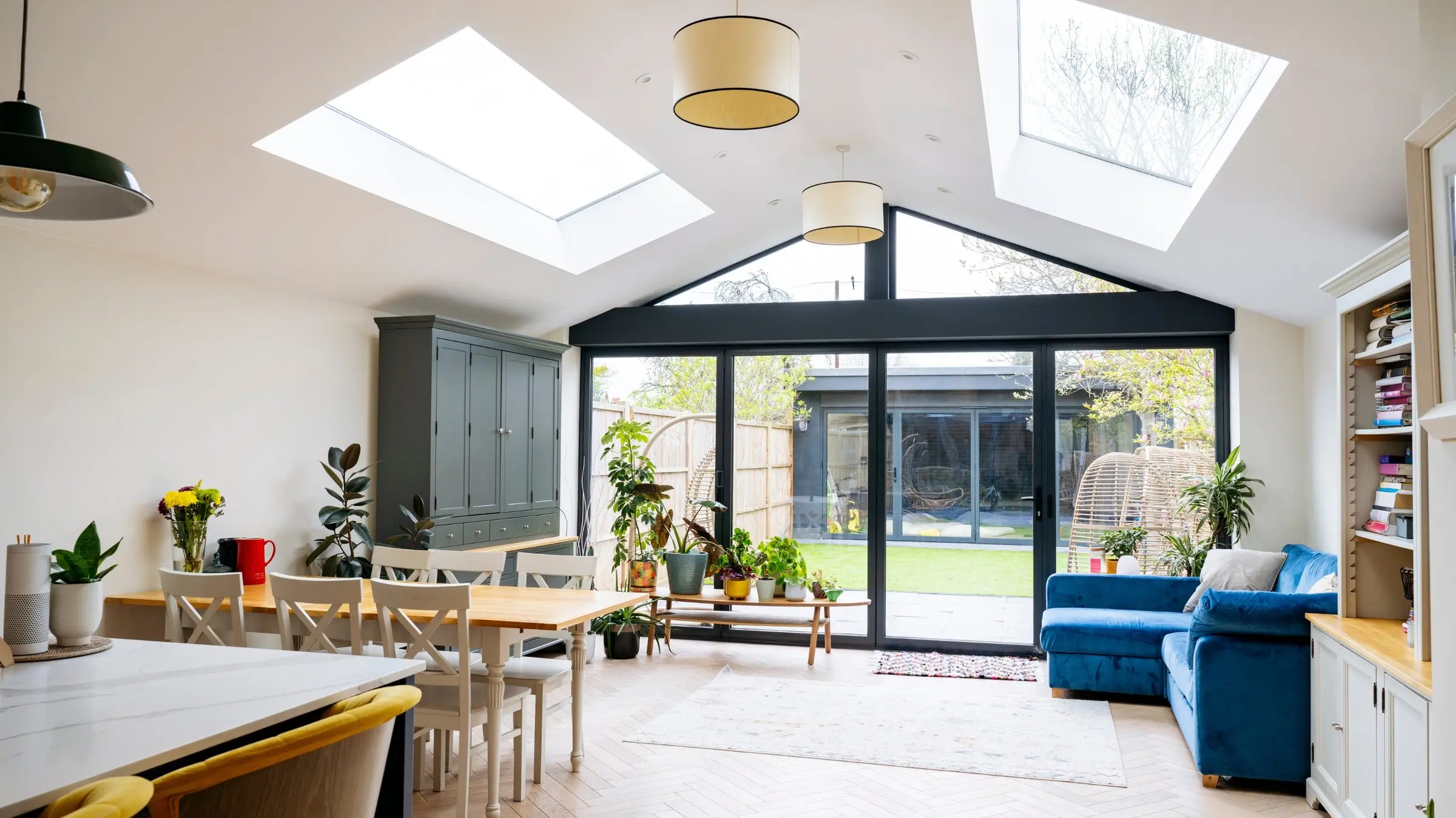 A bright open-plan holiday-let living space with skylights, a dining table set with flowers and garden doors, styled for its listing photographs