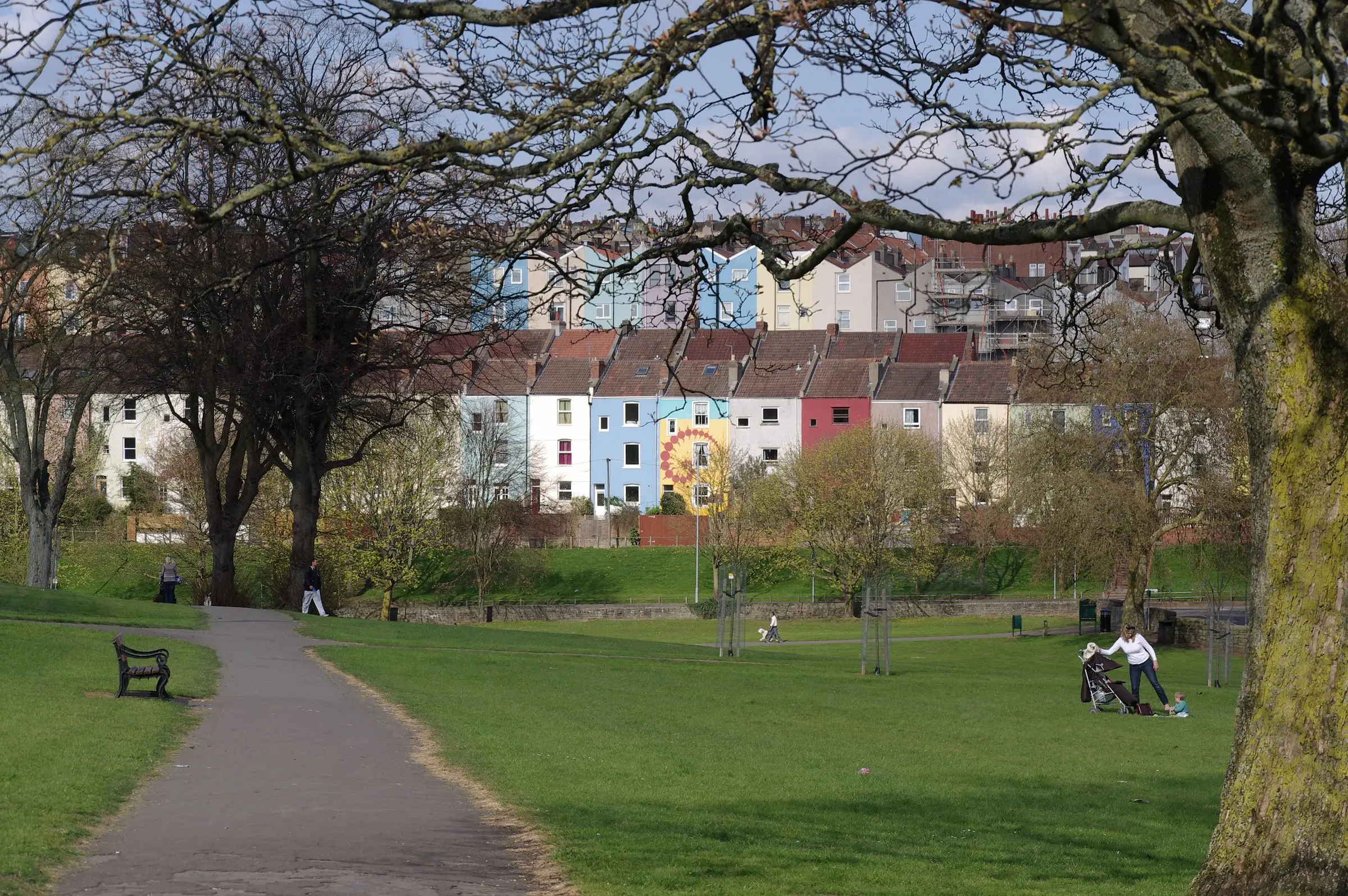 A row of brightly painted Bristol terraces seen across a green park from under the trees