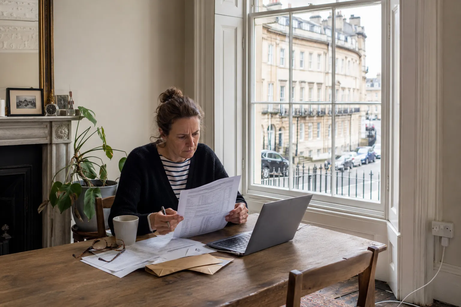 An owner reading an insurance policy schedule at a table by a tall sash window in a Georgian city flat