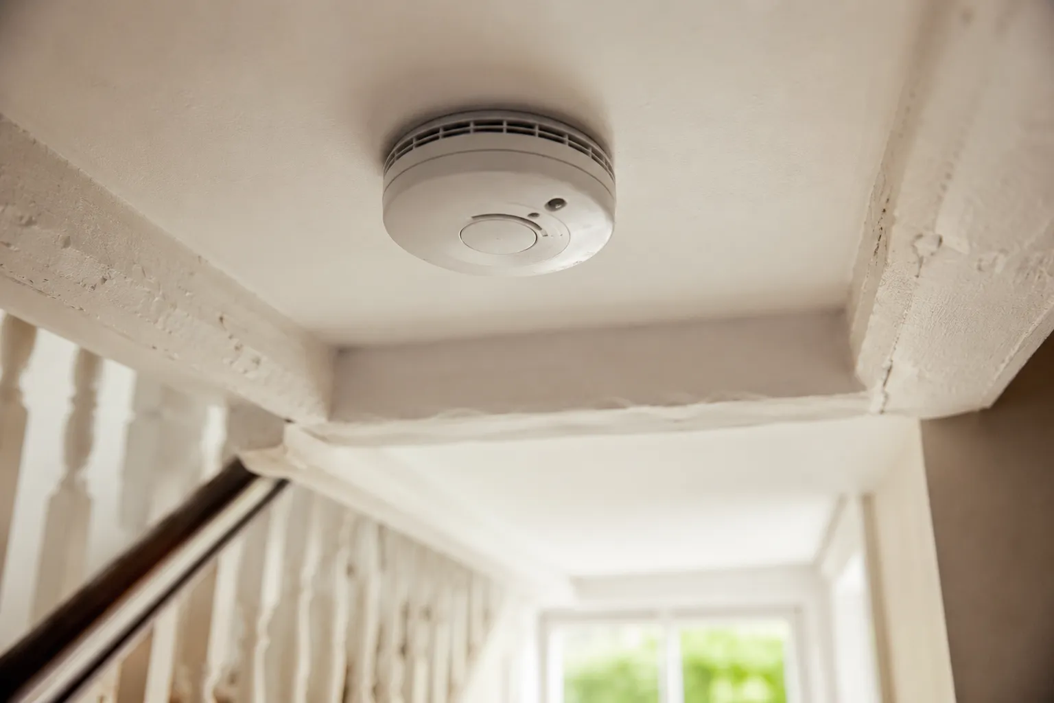 A white smoke alarm on a painted ceiling in a period cottage hallway